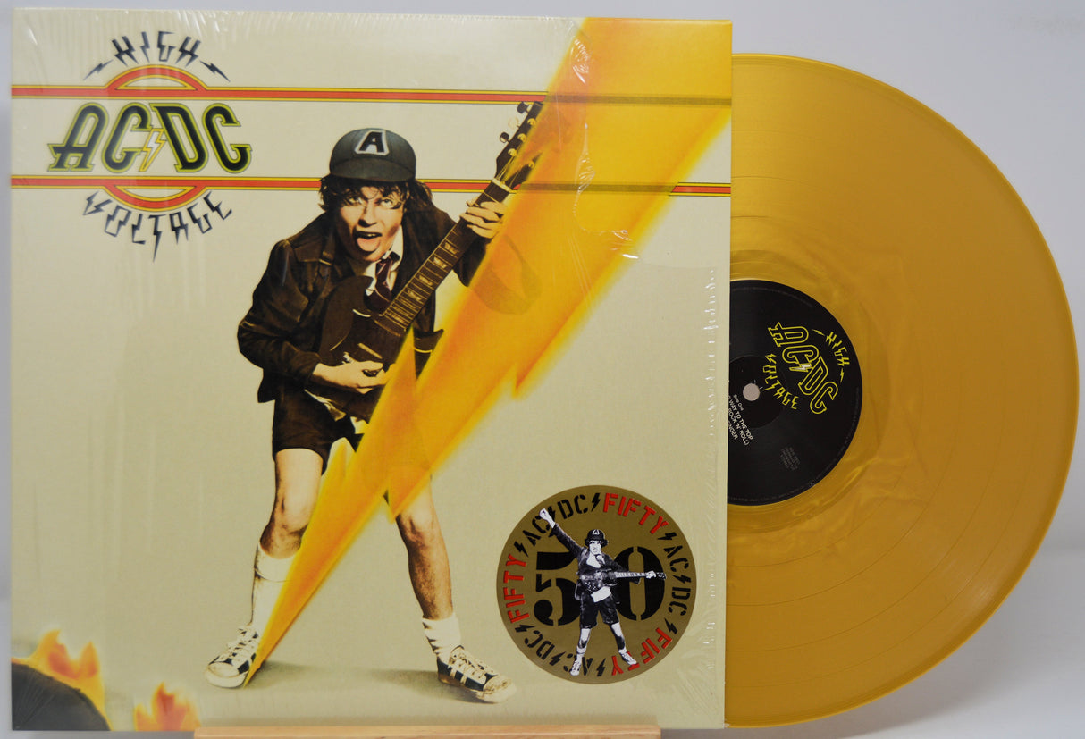 Gold vinyl record with AC/DC 'High Voltage' cover featuring a guitarist, on a white background