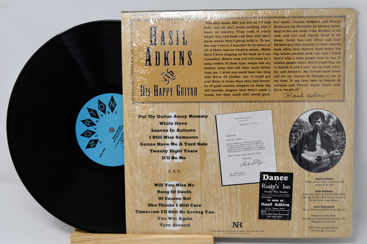 A vinyl record album of 'Achy Breaky Ha Ha Ha' by Hasil Adkins, with a picture of Hasil Adkins on the cover, placed on a record sleeve.