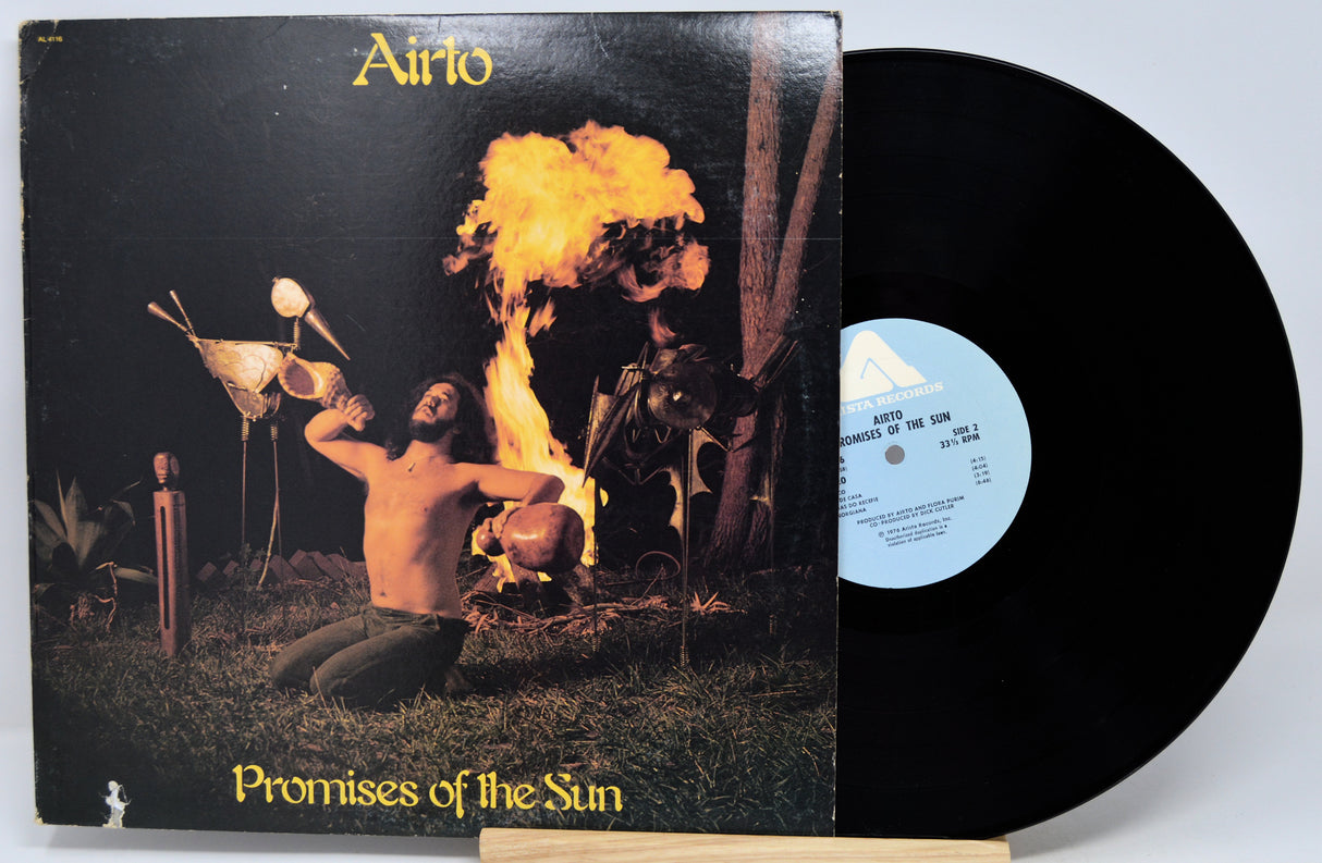 Airto 'Promises of the Sun' vinyl record LP with its illustrated album cover and the black vinyl record partially pulled out, displayed on a small wooden stand against a light gray background.