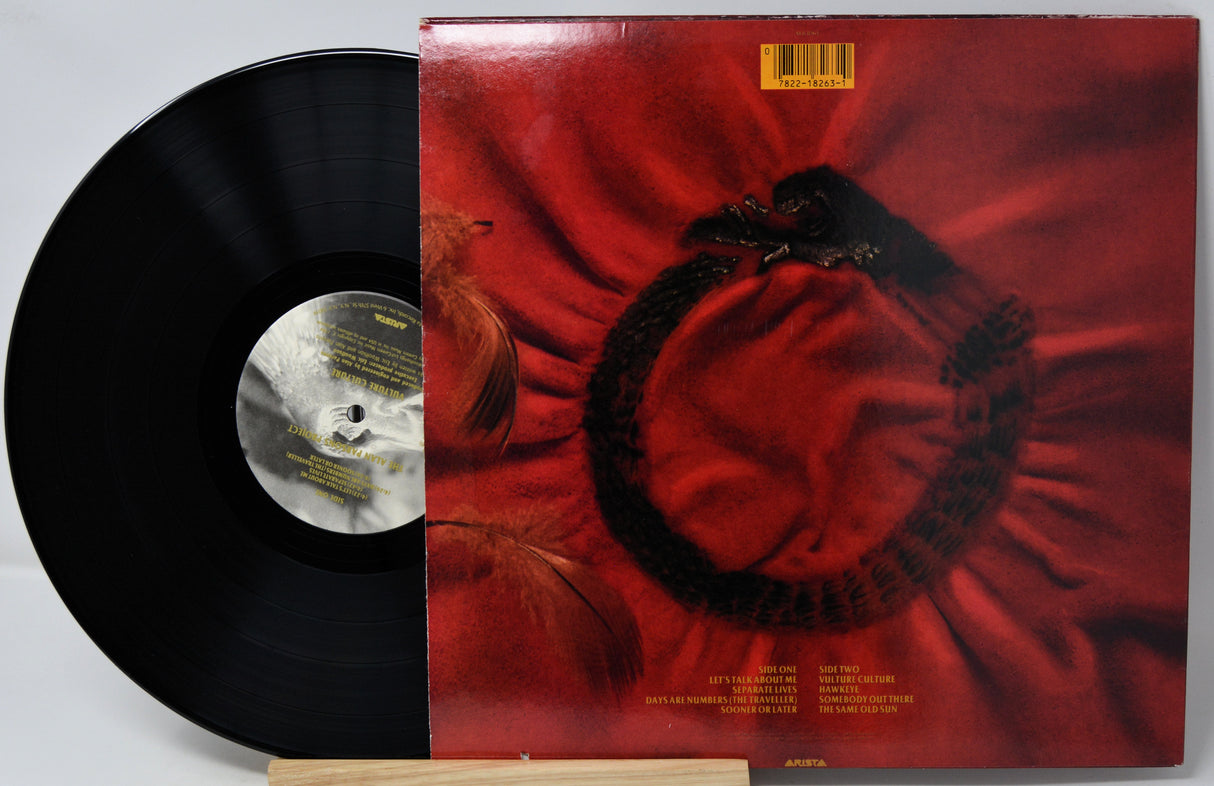 A vinyl record partially pulled from its album cover, showing a black record on the left and the cover on the right with a red abstract design and a black circular motif. The record label reads Columbia Records.