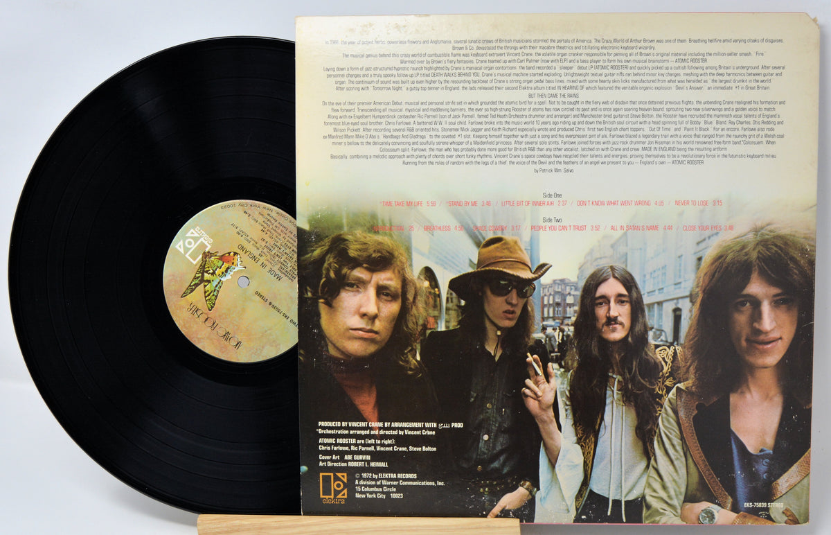 A vinyl record partially pulled from its sleeve, showing the black record on the left and the printed back cover on the right with band portraits and text.