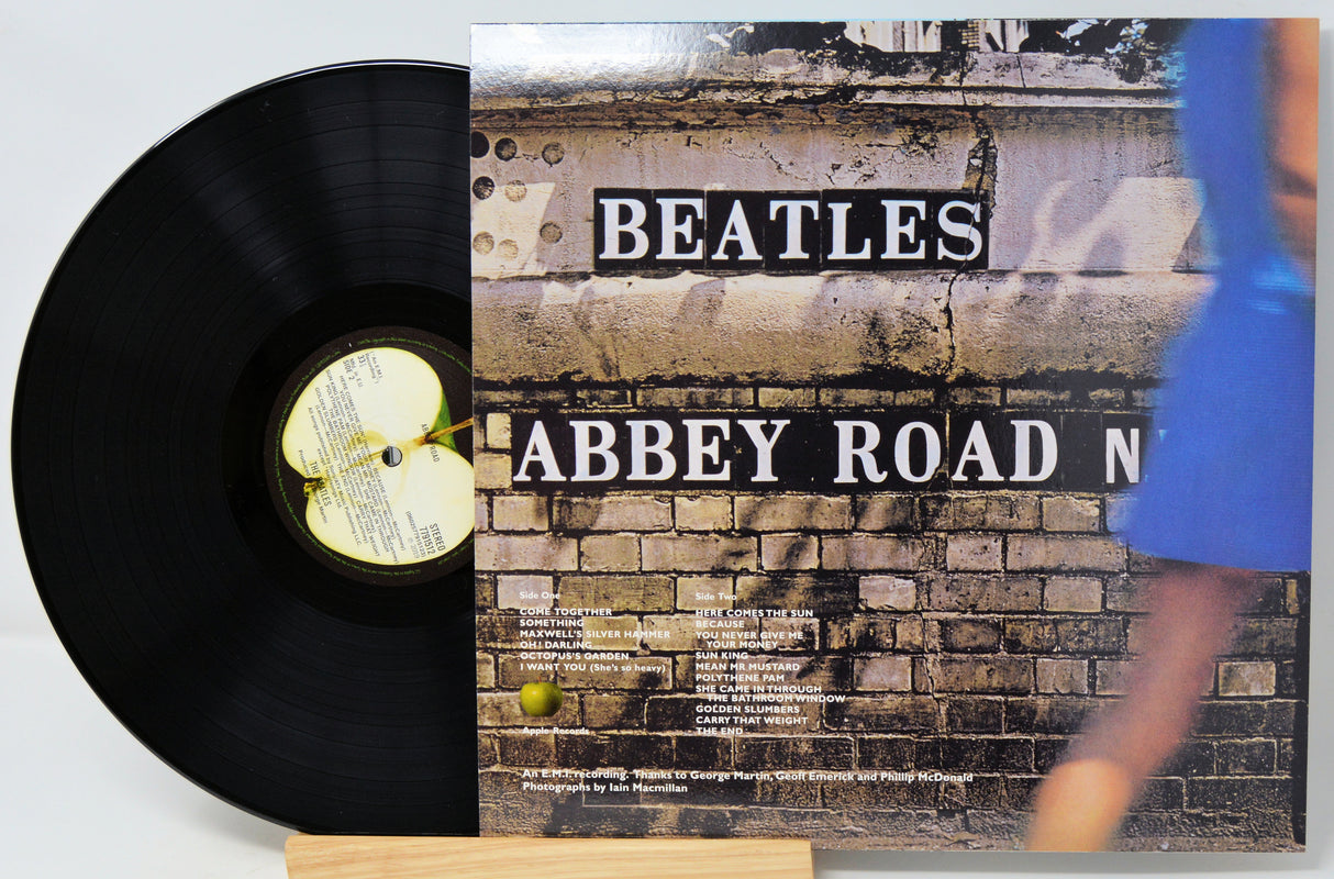 A Beatles 'Abbey Road' vinyl record partially pulled from its album cover, displayed on a small wooden stand against a light gray background.