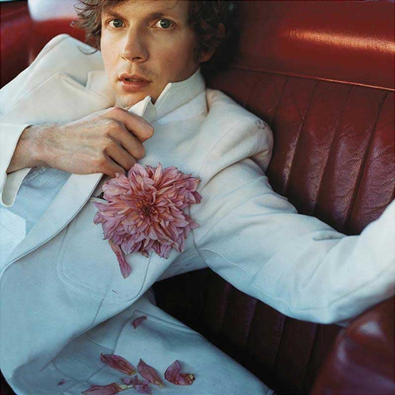 Person wearing a white coat with a pink flower, sitting on a red leather couch.