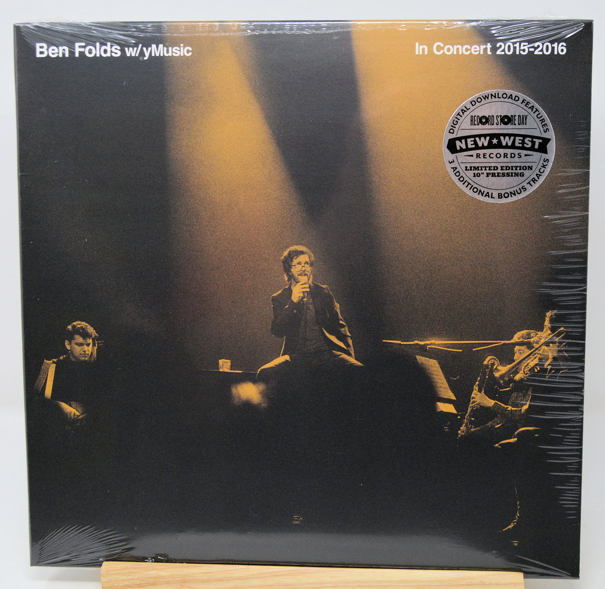 Ben Folds w/ y'music 'In Concert 2015-2016' vinyl record album, sealed in plastic shrink wrap, displayed on a wooden stand against a white background.