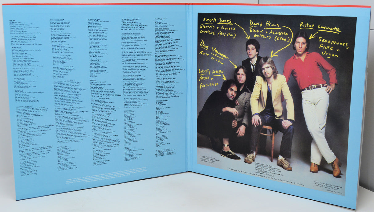 An open book or album cover spread showing a large printed portrait of four people on the right page with handwritten-style labels and arrows, and dense text printed across the left page on a light blue background.
