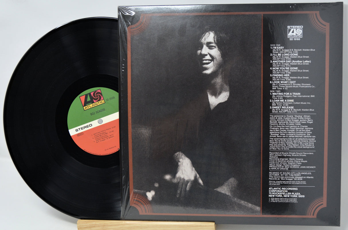 A vinyl record and its outer paper sleeve shown together on a light background. The sleeve features a black-and-white portrait of a smiling man and printed tracklist text, while the black record is partially pulled out and displays a colorful center label.