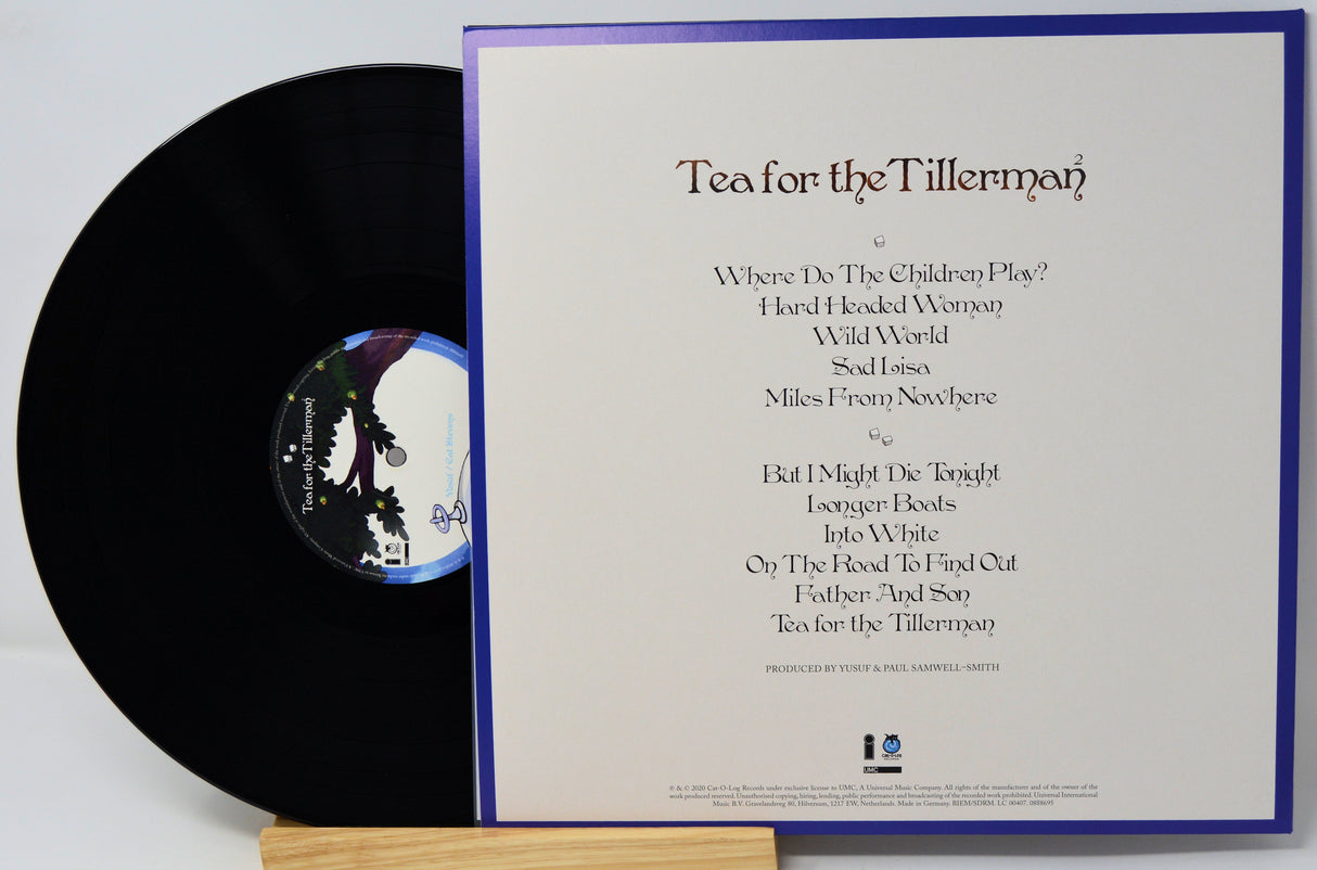 Vinyl record album shown with the black LP partially pulled from the sleeve, which displays the tracklist for Tea for the Tillerman. The sleeve has a white background with a purple border, and the record itself has a dark blue and white center label.