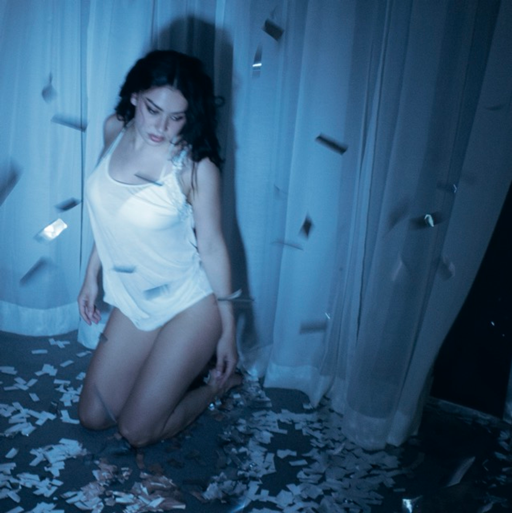 Charli SCS in a white outfit kneeling on a patterned floor with a blue tint.