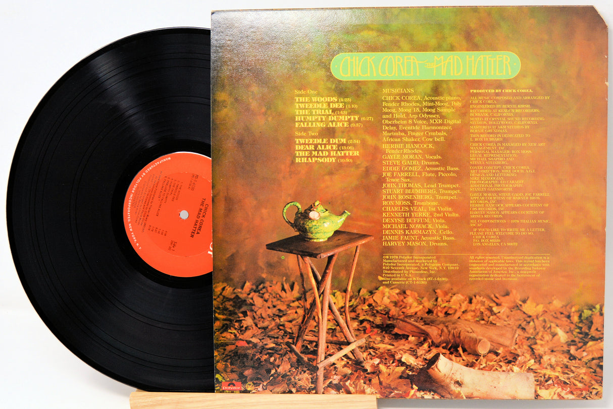 Vinyl record album shown with the black record partially pulled from the sleeve, photographed on a white background. The sleeve artwork features a warm autumn scene with orange and brown tones, a small green teapot on a table, and a list of track titles and artist names.