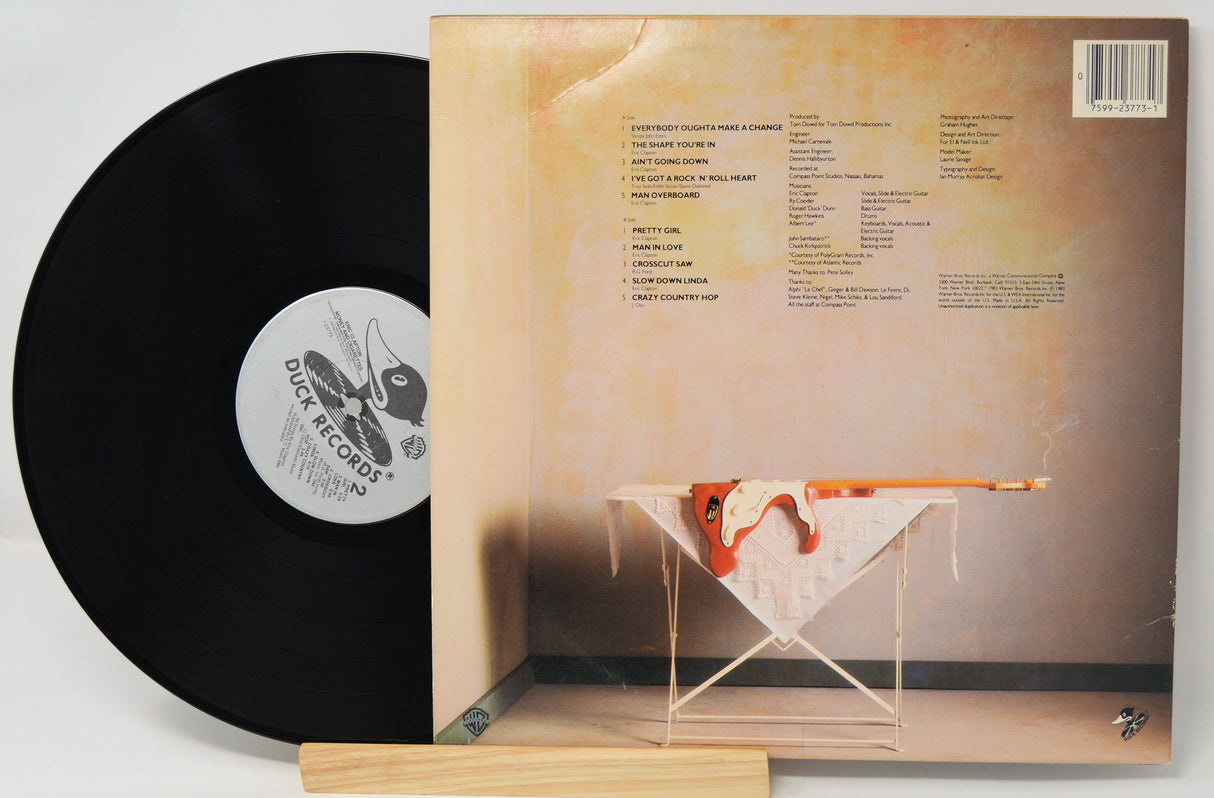 Vinyl record with cover featuring a table and abstract design, on a light gray background.