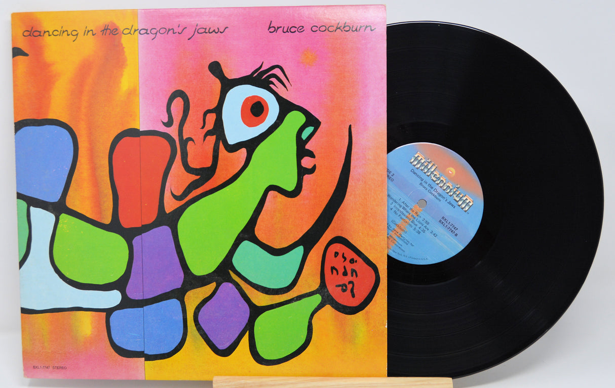 Vinyl record with colorful cover featuring a stylized face and text 'Dancing in the Dragon's Jaws' by Bruce Cockburn.