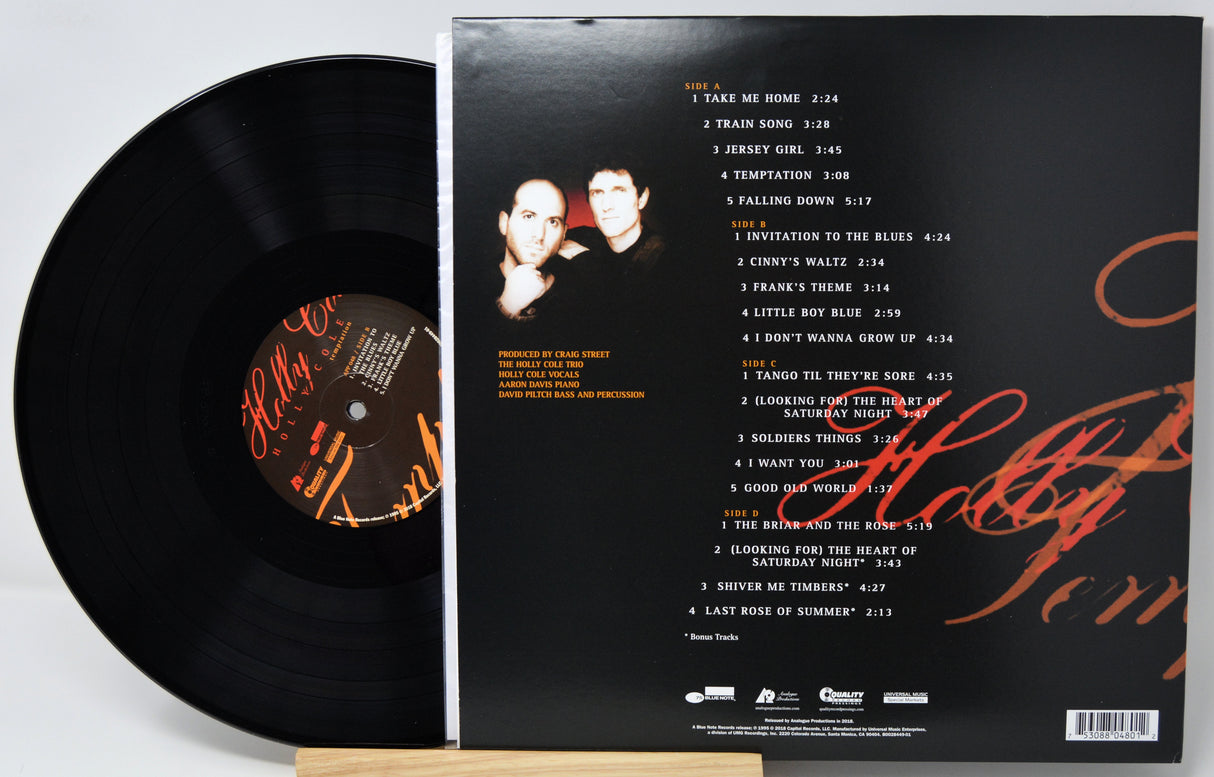 A vinyl record partially pulled from its black outer sleeve, showing the back of the packaging with tracklist text, a small portrait photo, and orange script artwork on a white background.