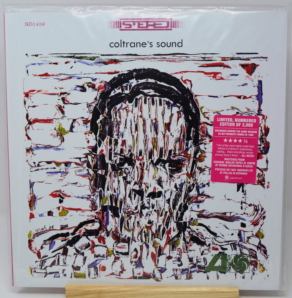 Vinyl record album cover for 'coltrane's sound' with a white background, abstract multicolor portrait artwork, a pink sticker on the right, and a small wooden display stand visible at the bottom.