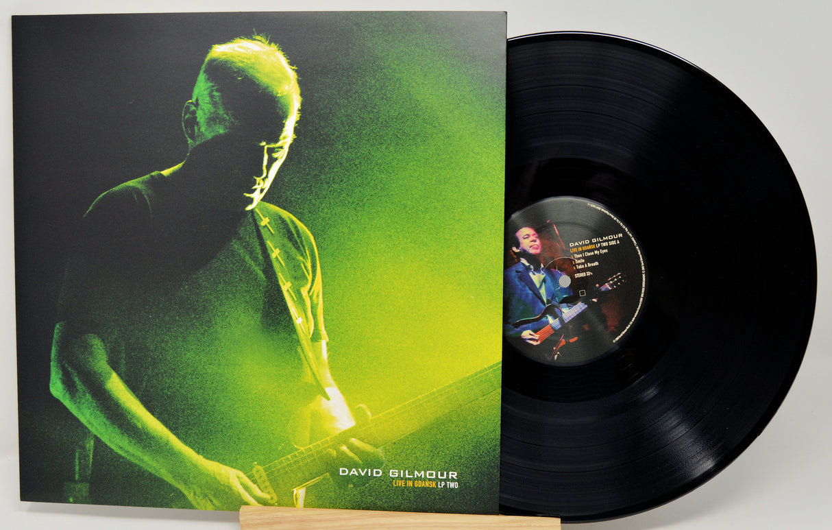 David Gilmour 'One Of These Nights' vinyl record LP with its illustrated album cover sleeve and the black vinyl disc partially pulled out, displayed on a small wooden stand against a light gray background.