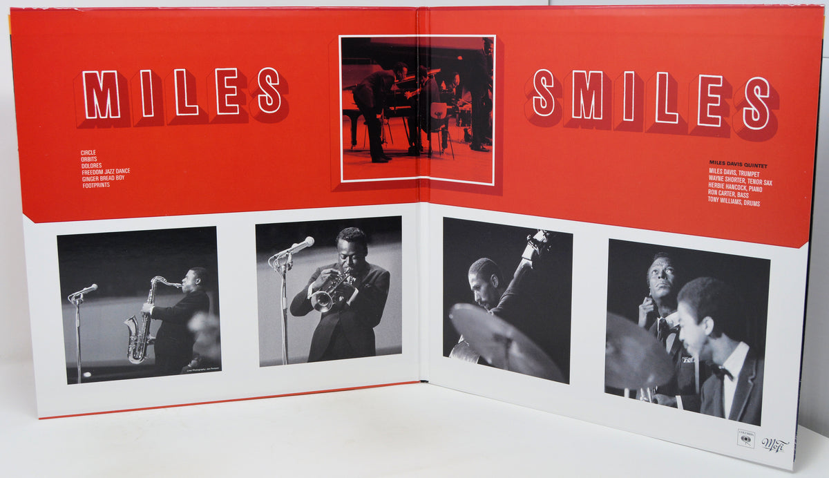 An open printed album or book spread titled "MILES SMILES" with a bold red header and multiple black-and-white photos of a musician performing, photographed on a white surface.