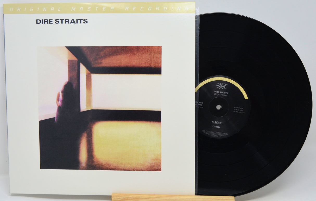Dire Straits 'Live at Leeds' vinyl record shown with its album cover sleeve and a black LP partially pulled out, displayed on a small wooden stand against a light gray background.