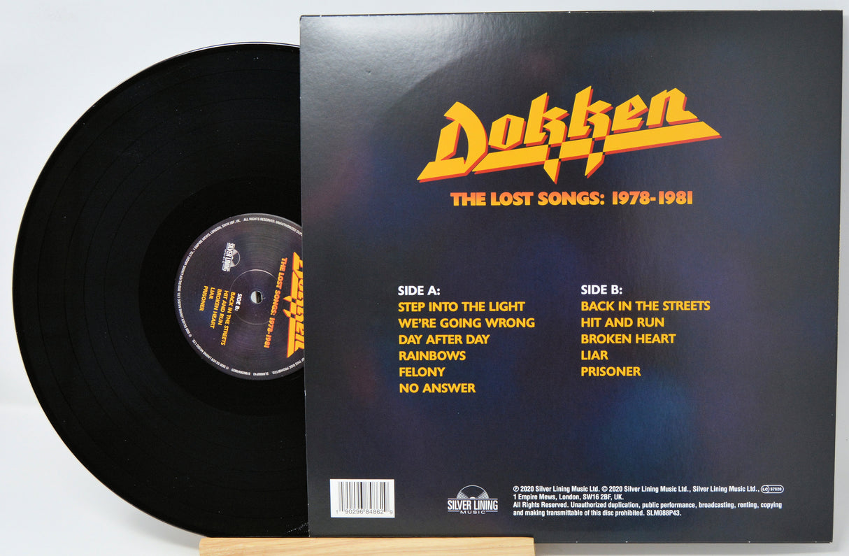 A black vinyl record partially pulled from its sleeve, showing the back cover of Dokken's 'The Lost Songs: 1978-1981' album. The sleeve has the band's name in large yellow/orange lettering and lists track titles for Side A and Side B on a dark background.