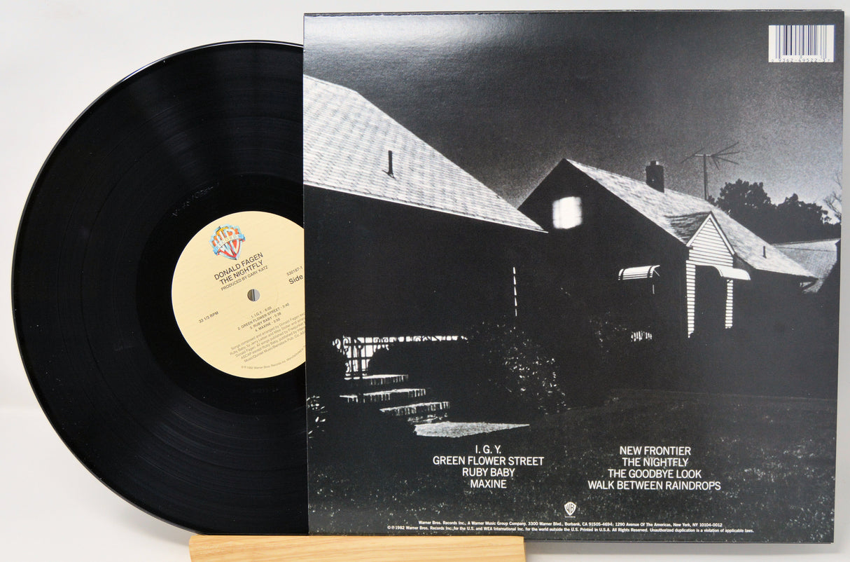 A vinyl record partially pulled from its sleeve, showing the black record on the left and the album cover on the right. The cover features a black-and-white photograph of a house and lists track titles including 'Green Flower Street' and 'New Frontier.