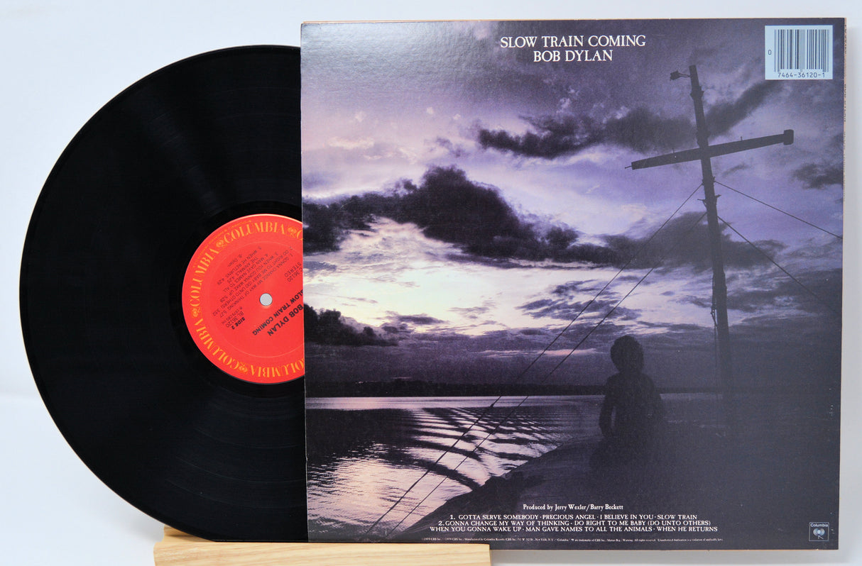 Vinyl record and back cover for Bob Dylan titled 'Slow Train Coming' showing someone sitting in a boat on the ocean at dusk.