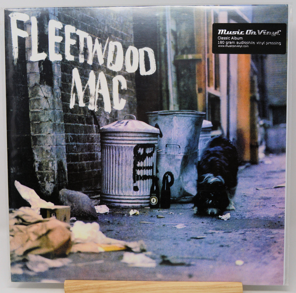 Fleetwood Mac 'Rumours' vinyl record album cover shown flat against a light background, with the band name in large white letters over a street scene featuring trash cans, a dog, and debris. A 'Music On Vinyl' sticker is visible in the top right.