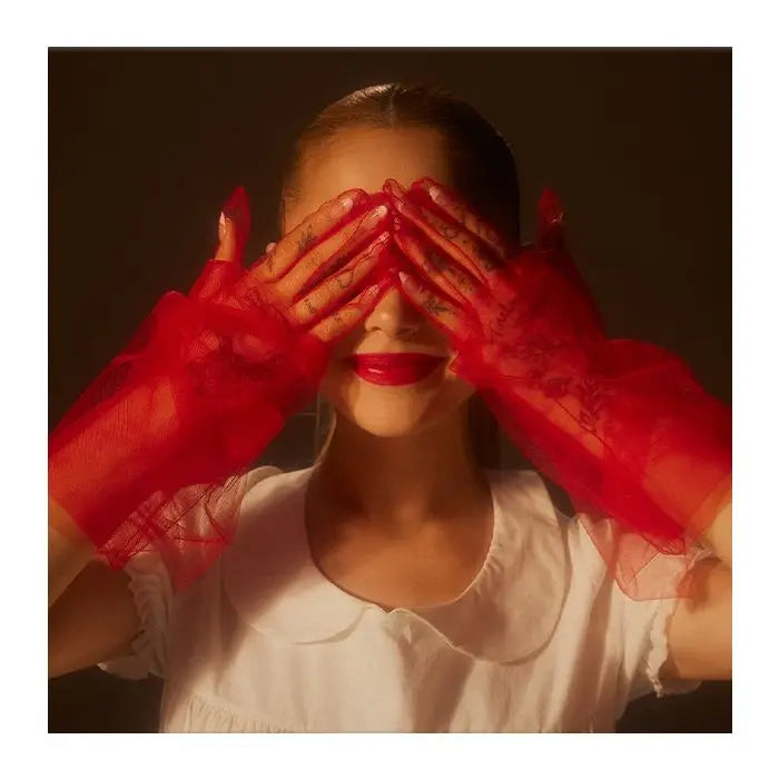 Ariana Grande with red vinyl gloves covering her eyes, wearing a white shirt.