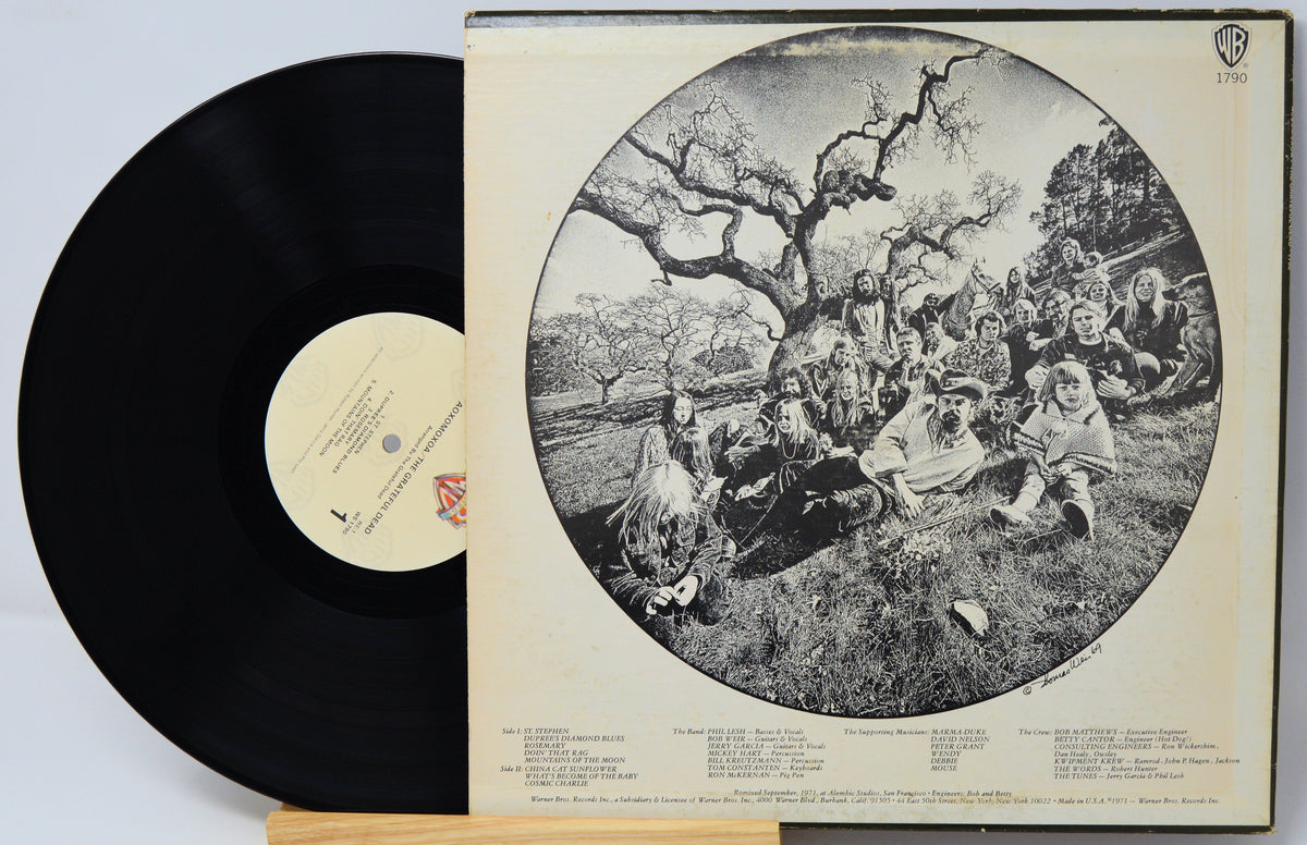 A vinyl record partially pulled from its sleeve, showing the black record on the left and the cream-colored album cover on the right with a large circular black-and-white band photograph and printed track listings.