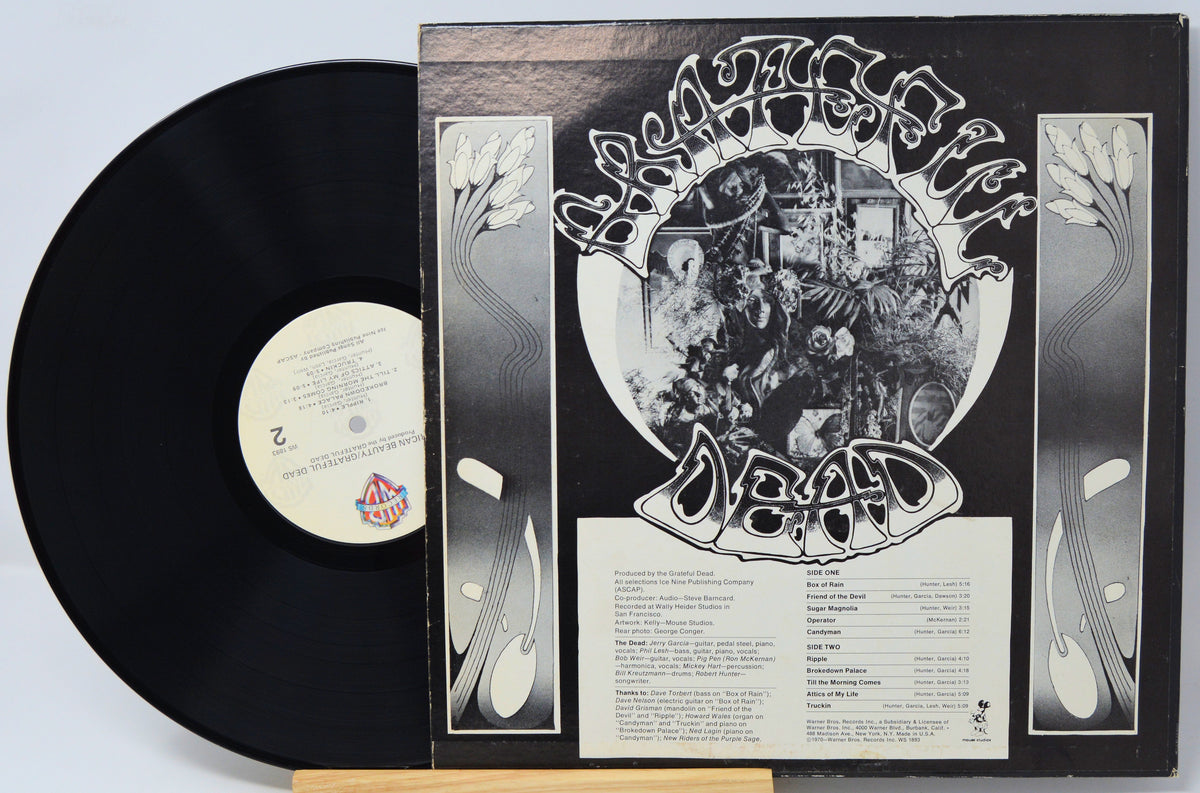 A vinyl record partially pulled from its sleeve, showing the black record, cream center label, and black-and-white album cover with stylized text and floral side panels.