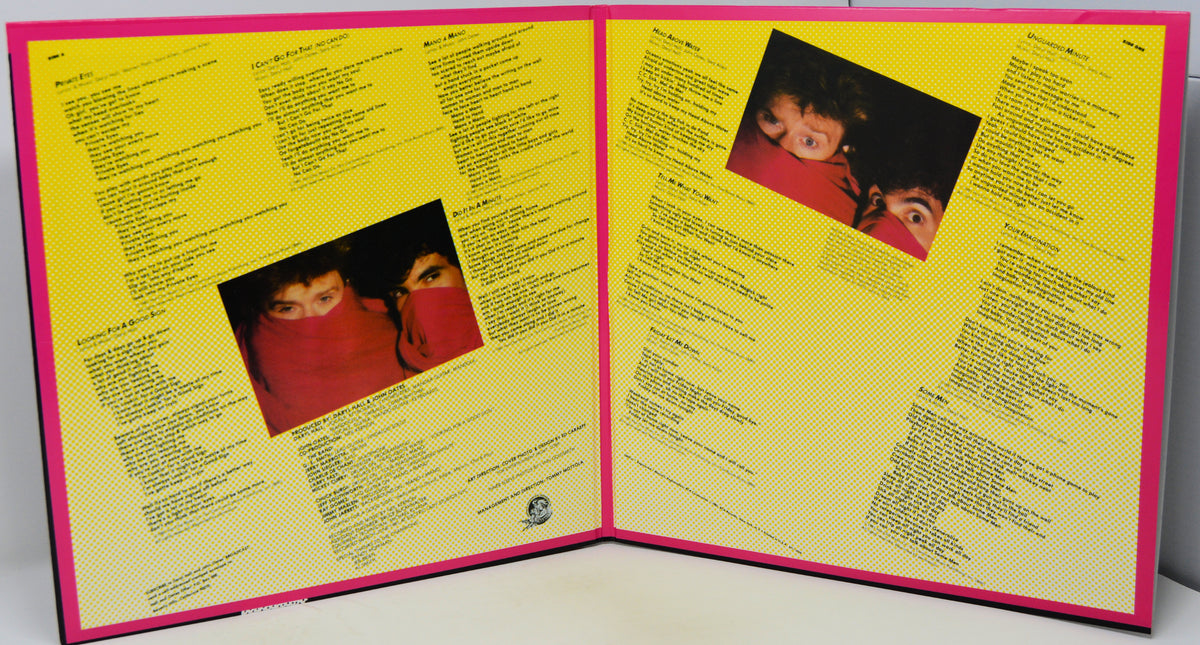 An open vinyl record sleeve or booklet with bright yellow printed pages, pink borders, and two small inset photos of a person in red clothing, photographed against a plain light background.