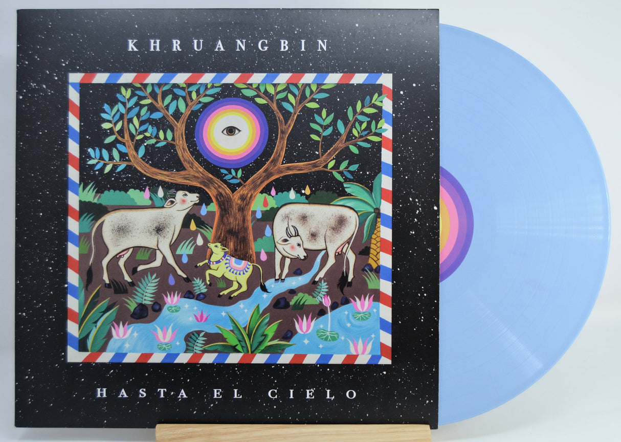 Front cover of Khruangbin's Hasta El Cielo blue vinyl with colorful tree, cows, and psychedelic eye artwork