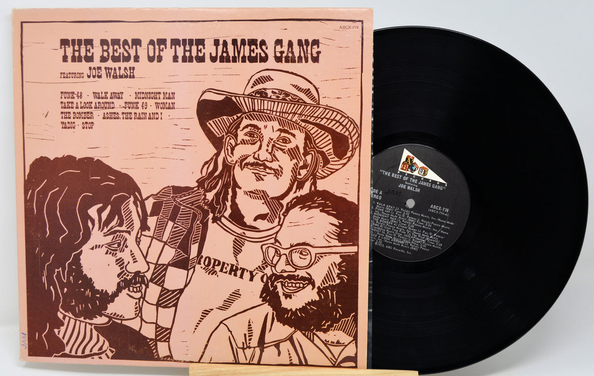 Vinyl record album cover and black record partially visible on a light gray background. The cover reads 'THE BEST OF THE JAMES GANG' with Joe Walsh credited, and features a sepia-toned illustrated portrait of three men.