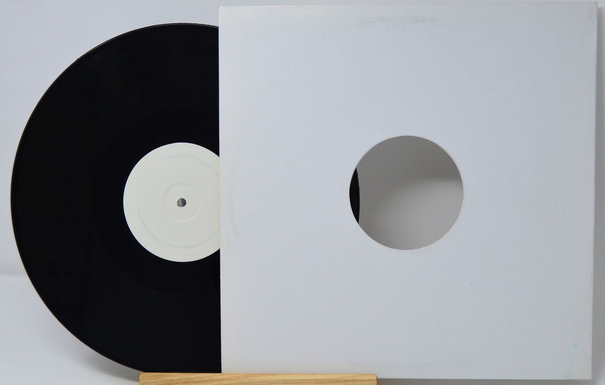 A black vinyl record partially pulled from a white square paper sleeve with a circular cutout, displayed against a light gray background.