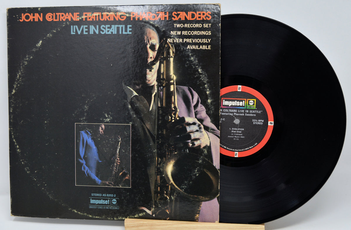 Impulse! Records 'John Coltrane Featuring Pharaoh Sanders - Live in Seattle' vinyl LP set, showing the illustrated album cover and the black vinyl record partially pulled out, resting on a small wooden stand.