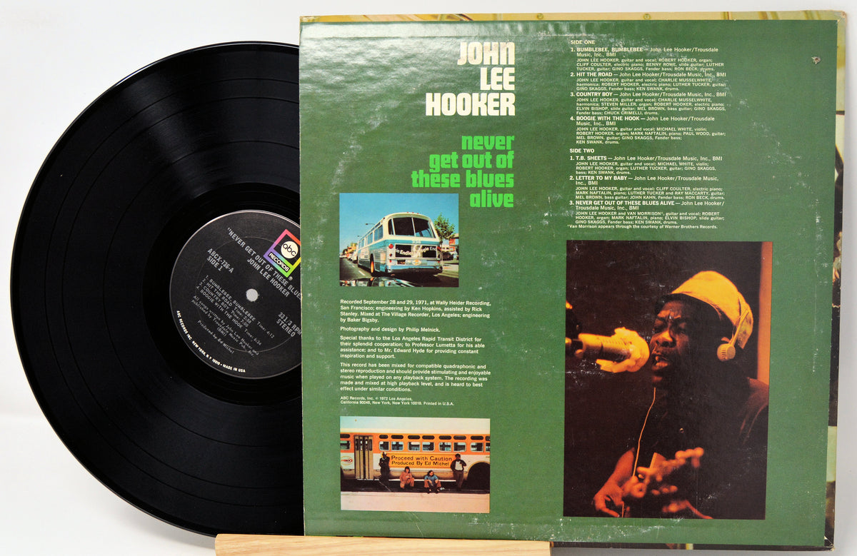 A vinyl record partially pulled from its sleeve, showing the black record on the left and the green album cover on the right. The cover features the text 'JOHN LEE HOOKER' and 'never get out of these blues alive,' along with printed photos and song listings.