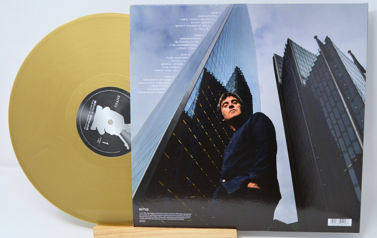 Johnny Marr posing beneath glass skyscrapers with tracklist, gold vinyl partially visible
