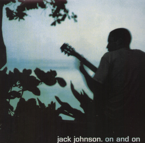 Silhouette of a person playing a guitar with a backdrop of tropical foliage and a body of water.