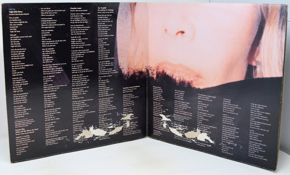 An open vinyl record sleeve or booklet showing printed track listings on both pages and a close-up photograph of a woman's face across the center, photographed against a plain light background.