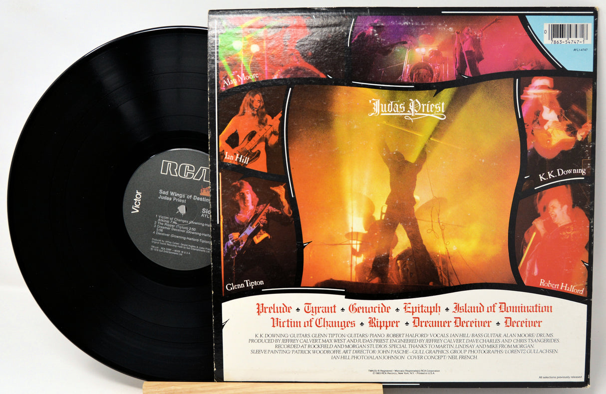 A vinyl record partially pulled from its sleeve, showing the black LP disc and the album cover for Judas Priest's 'Greatest Epics'. The cover features a collage of live performance photos with a fiery orange and yellow center, and the band's name is clearly visible.