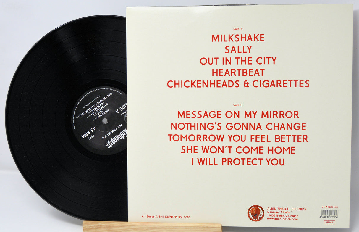 Vinyl record with white cover featuring red text on a light gray background