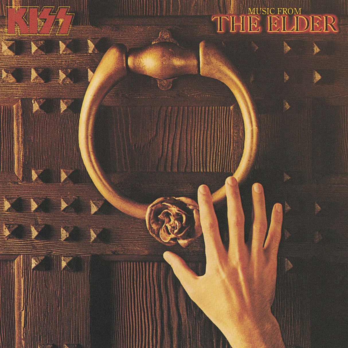 A vinyl record titled 'Kiss - Music from the Elder' with an image of a hand holding a large, gold-colored ring on a dark, wooden door.