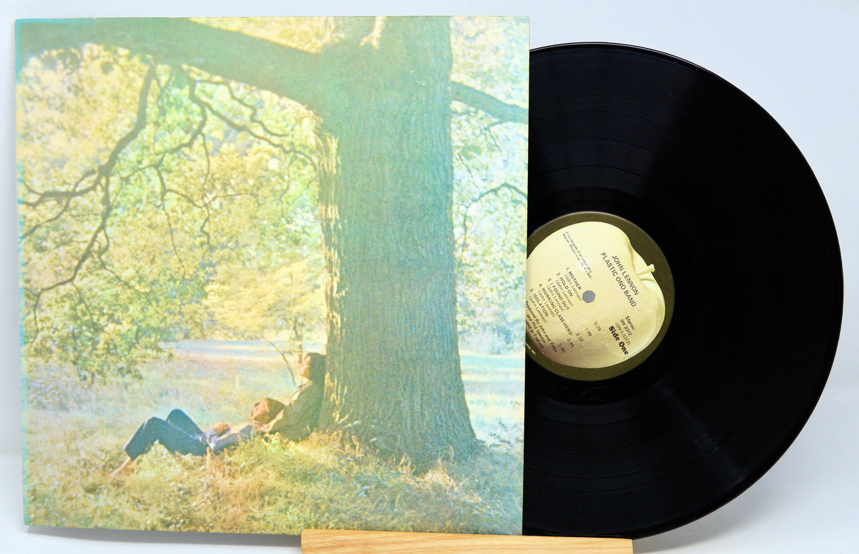 A vinyl record of John Lennon's Plastic Ono Band album placed next to its cover, which features an image of John Lennon lying under a tree.