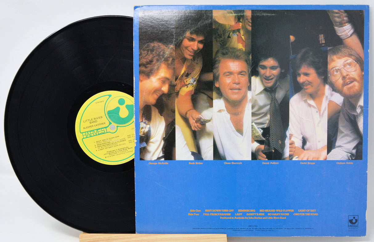 A vinyl record partially pulled from its sleeve, showing the black record and the blue album cover with a collage of five people and a yellow center label.