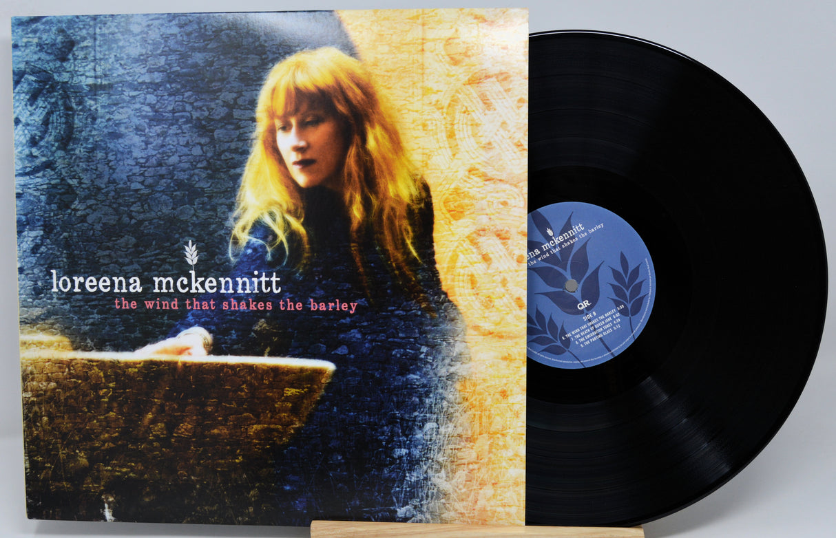 A vinyl record partially pulled from its album sleeve, showing the cover art for Loreena McKennitt's 'The Wind That Shakes the Barley'. The sleeve features a textured split design of dark blue and golden yellow, with a portrait of the artist.