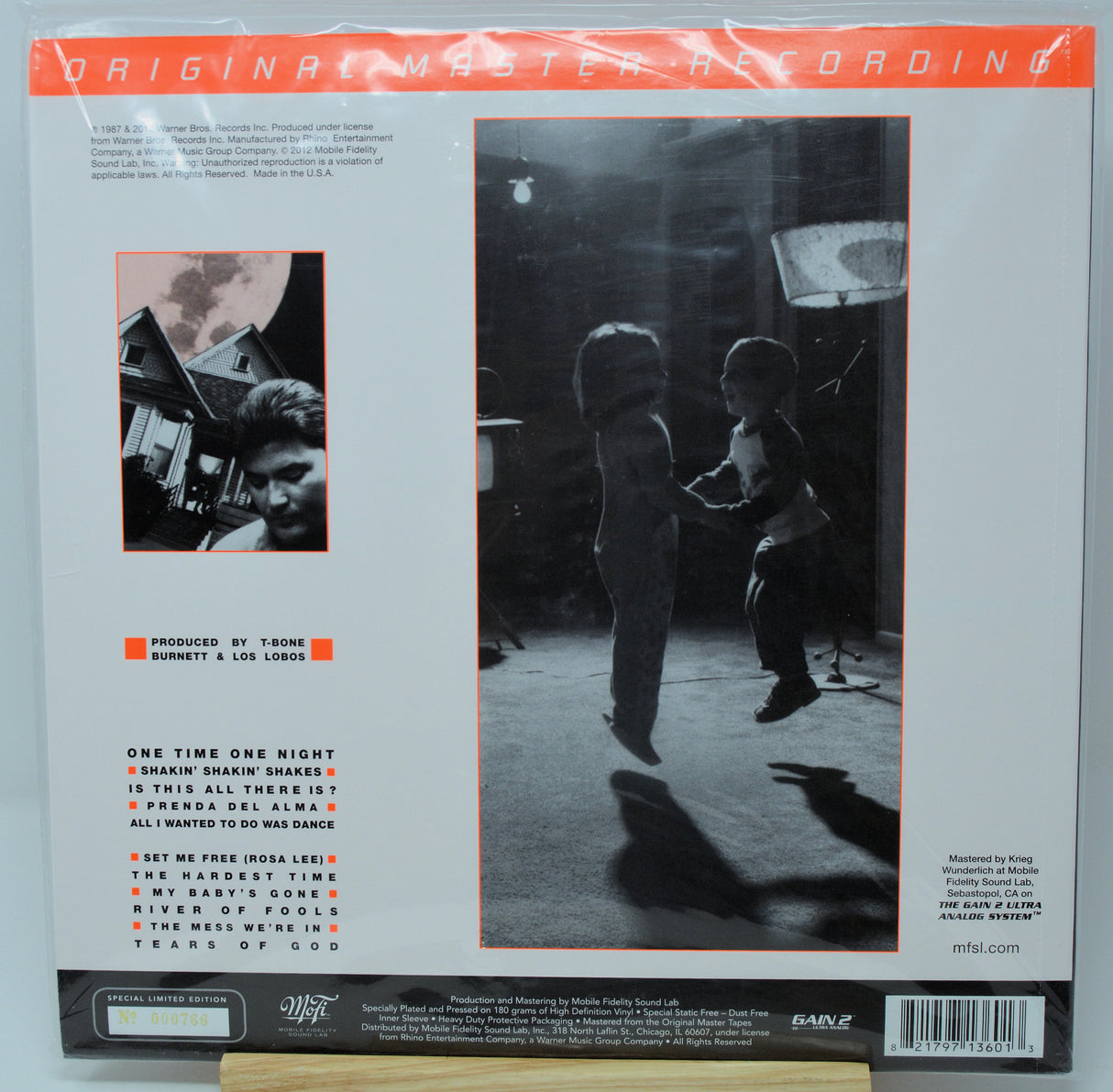 Back cover of a vinyl record sleeve for 'One Time One Night' by Bushbaby & Los Logos, featuring a large black-and-white photo of two children in a dark room, track listing text, and orange accents on a white background.