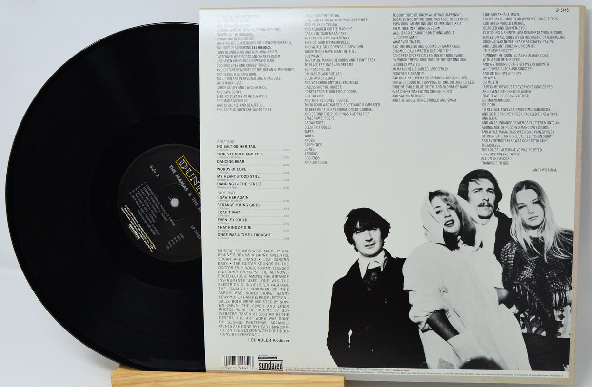 A vinyl record partially pulled from its open back cover sleeve, showing the black record on the left and the printed inner sleeve back with track listings and a black-and-white group photo on the right.