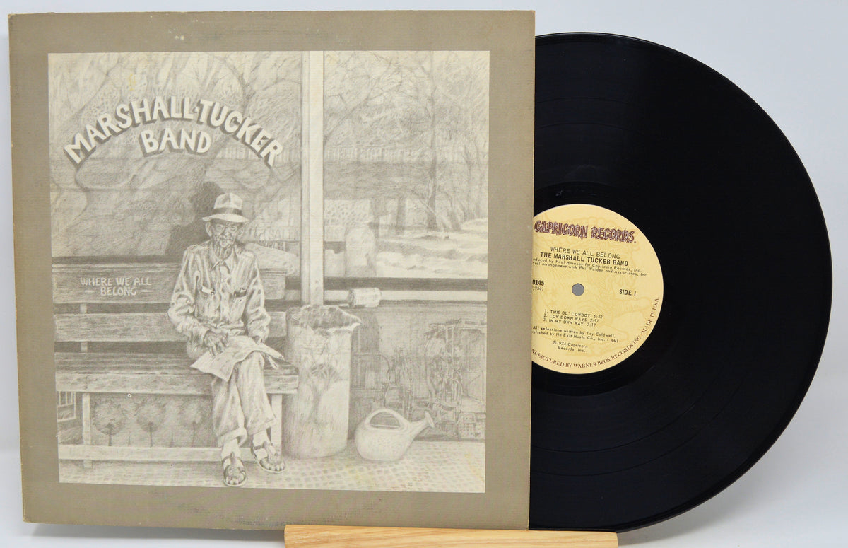 A vinyl record and its album cover for Marshall Tucker Band's 'Where We Fle Wagon' are displayed on a small wooden stand against a light gray background.