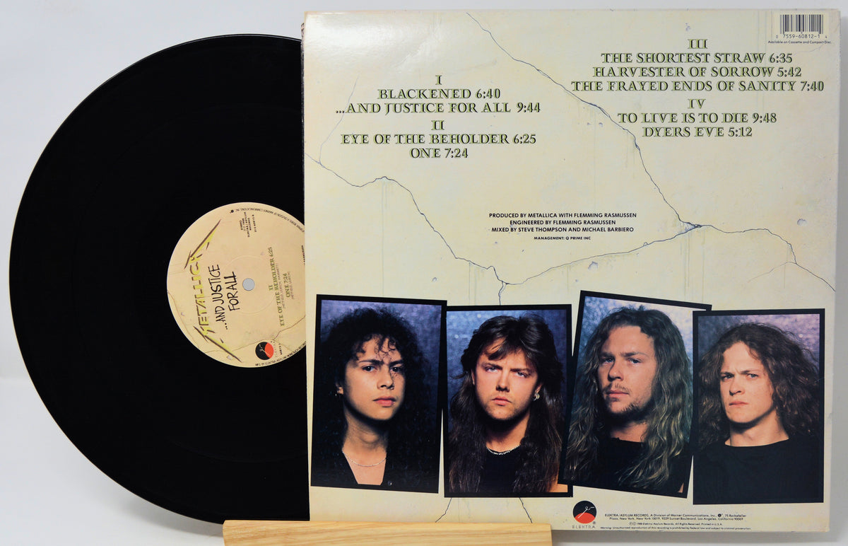 A vinyl record partially pulled from its sleeve, showing the black disc and the printed album cover. The cover includes the tracklist and four portrait photos of band members.