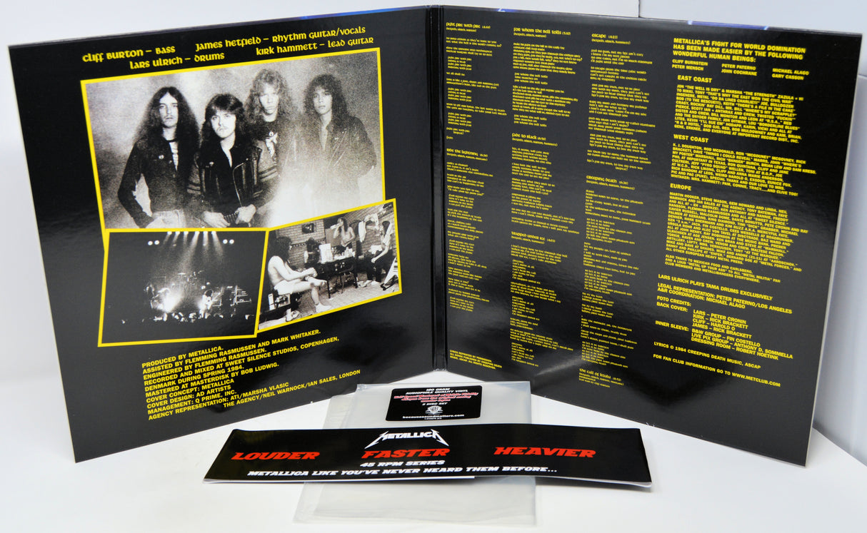 Metallica 'Heavier Than Never' CD album package shown open to the back insert, with printed black-and-white band photos, tracklist text in yellow, and a small printed card in front on a white background.