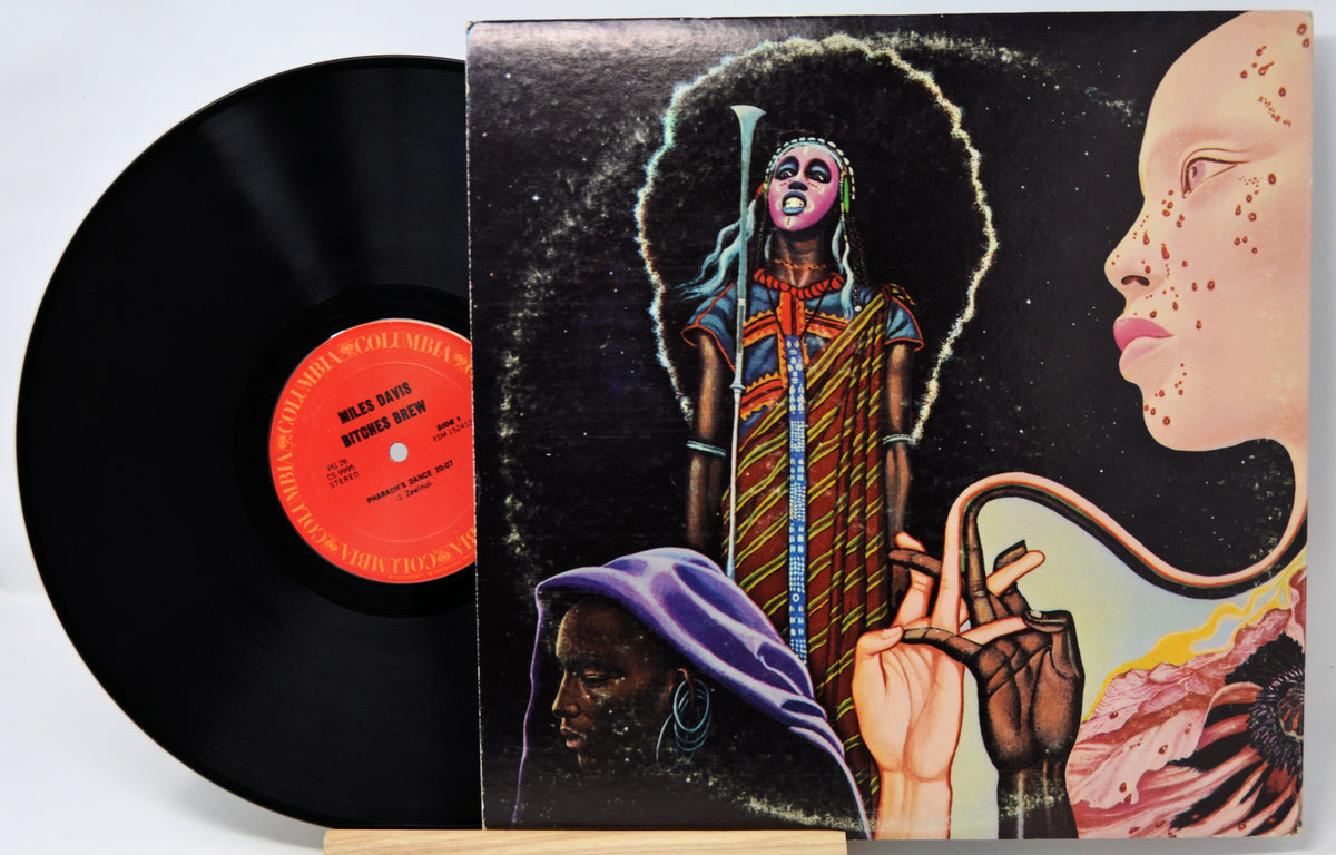 A vinyl record partially pulled from its illustrated album cover, showing the black record and a colorful cover with surreal portrait artwork and a red-orange center label.