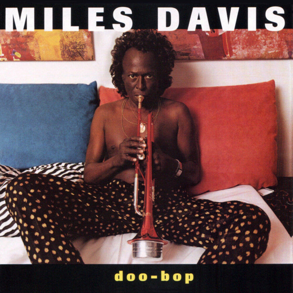 Album cover featuring Miles Davis playing a trumpet on a bed with colorful pillows.