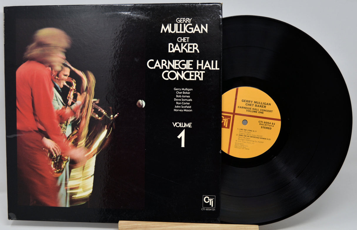 Vinyl record album 'Carnegie Hall Concert Volume 1' by Gerry Mulligan and Chet Baker, showing the black cover with a performer photo and the black record partially pulled out, displayed on a stand against a light gray background.